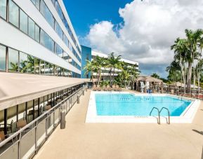 Sonesta Miami Airport’s outdoor pool has palm trees nearby, with tables and chairs, and sun loungers, by the side.