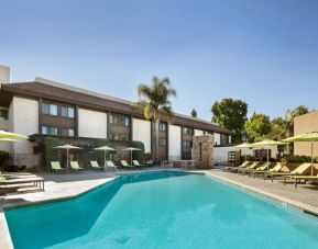 The outdoor pool of Sonesta Silicon Valley has nearby sun loungers, tables and chairs, and plenty of shade available.