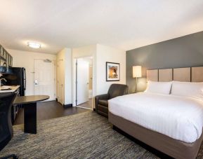 Sonesta Simply Suites Cleveland North Olmsted Airport double bed guest room, featuring armchair, desk, and kitchenette.