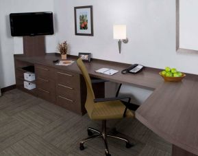 Sonesta Simply Suites Albuquerque guest room workspace, featuring desk, chair, telephone, lamp, and nearby TV.