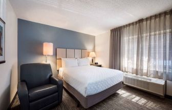 Double bed guest room in Sonesta Simply Suites Nashville Brentwood, featuring armchair, bedside lamp, and window.