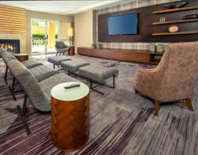 The hotel lobby is furnished with a very large TV, comfortable seating with footstools, a fireplace, and coffee tables.