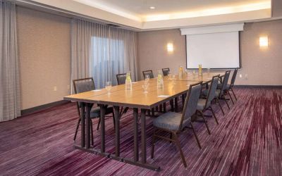 Sonesta Select Allentown Bethlehem Airport meeting room, including long wooden table, projector screen, seating for eight, and window.