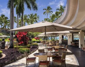 The hotel’s terrace includes dining under shaded cover, with the pool and towering trees nearby.