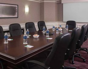 Sonesta Select Boston Lowell Chelmsford meeting room, including long wooden table, nine leather swivel chairs, and a projector screen.