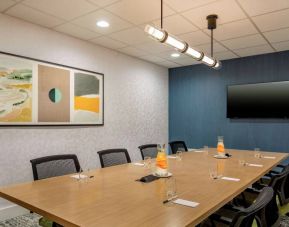 Meeting room in Sonesta Select Boston Foxborough Mansfield with long wooden table, eight chairs, and a large, wall-mounted TV.