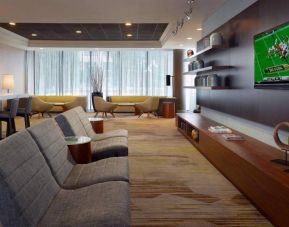 Sonesta Select Atlanta Cumberland Galleria’s lobby has a large, wall-mounted TV, comfortable seating, and coffee tables.