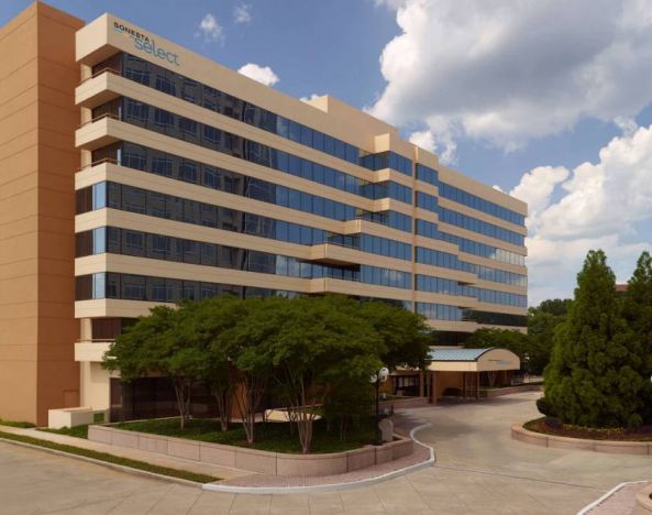 Sonesta Select Atlanta Cumberland Galleria’s exterior has the name on the building, numerous trees, and a covered entranceway.