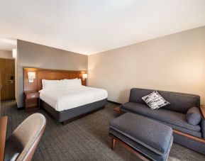 Double bed guest room in Sonesta Select San Jose Airport, furnished with sofa, chair, and TV.