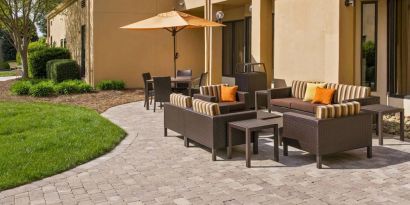 The patio at Sonesta Select Charlotte University Research Park includes sofa and armchair seating, plus coffee tables, near to pleasant greenery.