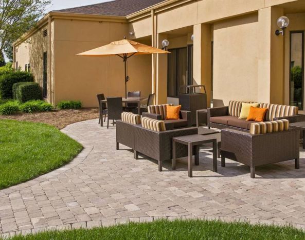 The patio at Sonesta Select Charlotte University Research Park includes sofa and armchair seating, plus coffee tables, near to pleasant greenery.