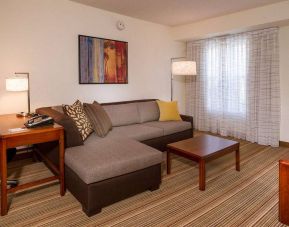 Sonesta ES Suites Charlottesville University guest room living area, including corner sofa, coffee table, TV, and window.