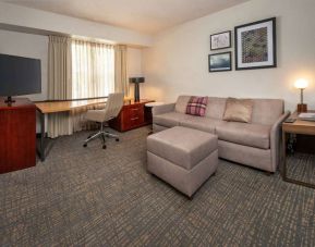 Sonesta ES Suites Baltimore BWI Airport guest room workspace, featuring chair, desk, and TV, plus a sofa nearby.