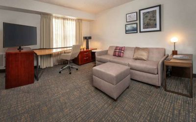 Sonesta ES Suites Baltimore BWI Airport guest room workspace, featuring chair, desk, and TV, plus a sofa nearby.
