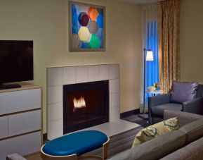 Sonesta ES Suites Cincinnati - Blue Ash guest room lounge, furnished with sofa, armchair, TV, and fireplace.