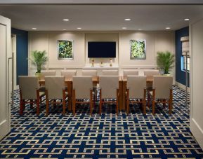 Hotel meeting room, decorated with potted plants and wall art, and featuring a dozen chairs around a long table.