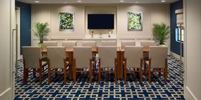 Hotel meeting room, decorated with potted plants and wall art, and featuring a dozen chairs around a long table.