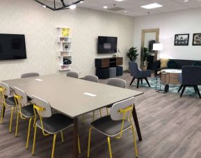 Sonesta Miami Airport meeting room facility, with long table, wall-mounted TV, and nearby armchair and sofa seating. 