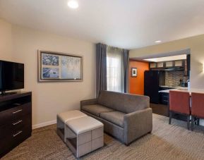 Guest room in Sonesta ES Suites Dulles Airport, featuring sofa and widescreen TV, with nearby kitchenette.