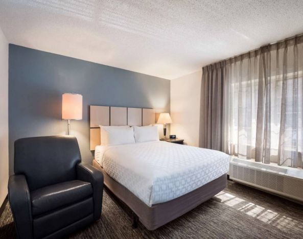 Double bed guest room in Sonesta Simply Suites Cleveland North Olmsted Airport, including armchair and windows.