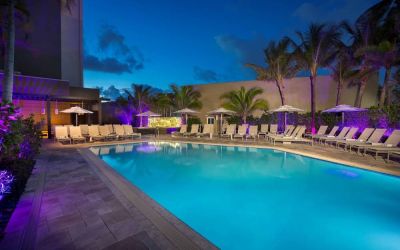 Sonesta Fort Lauderdale Beach’s outdoor pool has palm trees and sun loungers by the side, with shade available.