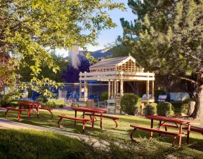 The picnic area at Sonesta ES Suites Flagstaff features benches on tables on grass, with trees and and barbecue facilities nearby.