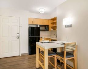 Sonesta ES Suites Charlotte Arrowood guest room kitchen area, with fridge-freezer, small table, sink, oven, and microwave.