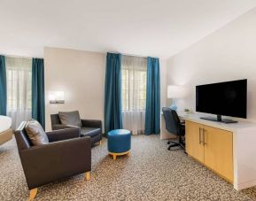 Sonesta ES Suites Charlotte Arrowood guest room workspace desk and chair, with nearby armchairs and television.