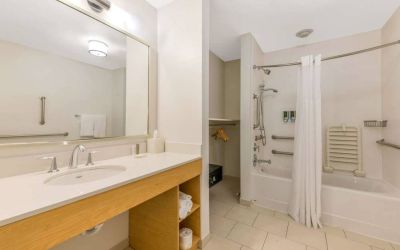 Guest bathroom in Sonesta ES Suites Charlotte Arrowood, furnished with large mirror, sink, bath and shower.