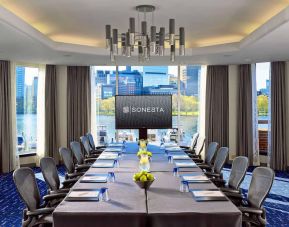 Royal Sonesta Boston meeting room, featuring large windows and high ceiling, long table and twelve surrounding chairs, plus widescreen TV.