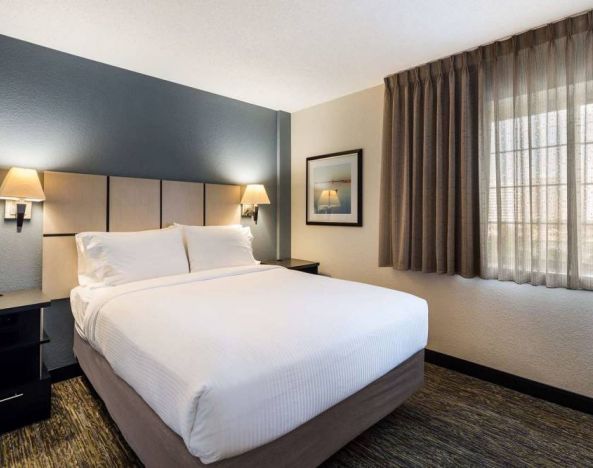 Sonesta Simply Suites Chicago Waukegan double bed guest room, featuring bedside lamps, art on the wall, and window.
