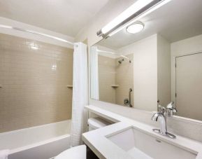 Guest bathroom in Sonesta Simply Suites Des Moines, including a long mirror, lavatory, sink, and bath with a shower.
