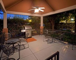 Sonesta Simply Suites Dallas Galleria’s barbecue area features tables and chairs under cover, with barbecue facilities and nearby trees.