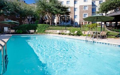 Sonesta ES Suites Austin The Domain Area’s outdoor pool features tables and chairs by the side, some of which are shaded, and nearby trees.
