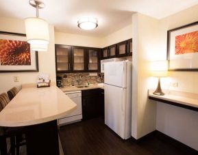 Sonesta ES Suites Austin The Domain Area guest room kitchen, including fridge-freezer, microwave, and breakfast bar with two stools.