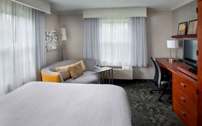 Double bed guest room in Sonesta Select Tinton Falls Eatontown, including workspace desk and chair, sofa, TV, and windows.