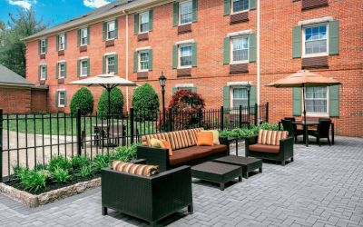 Sonesta Select Tinton Falls Eatontown’s patio is furnished with shaded tables and chairs, in addition to sofa and armchair seating, with greenery nearby.