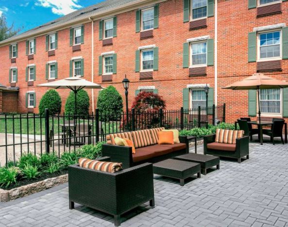 Sonesta Select Tinton Falls Eatontown’s patio is furnished with shaded tables and chairs, in addition to sofa and armchair seating, with greenery nearby.