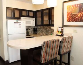 Guest room kitchen in Sonesta ES Suites Portland Vancouver 41st Street, featuring fridge-freezer, microwave, breakfast bar and two stools.