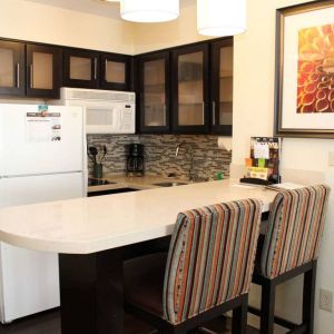 Guest room kitchen in Sonesta ES Suites Portland Vancouver 41st Street, featuring fridge-freezer, microwave, breakfast bar and two stools.