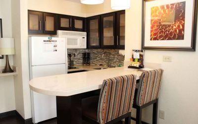 Guest room kitchen in Sonesta ES Suites Portland Vancouver 41st Street, featuring fridge-freezer, microwave, breakfast bar and two stools.