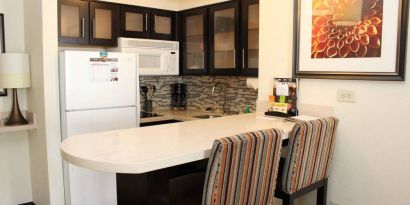 Guest room kitchen in Sonesta ES Suites Portland Vancouver 41st Street, featuring fridge-freezer, microwave, breakfast bar and two stools.