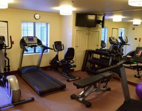 The fitness center of Sonesta ES Suites Portland Vancouver 41st Street has rows of free weights, a wall-mounted TV, and a variety of xercise machines.