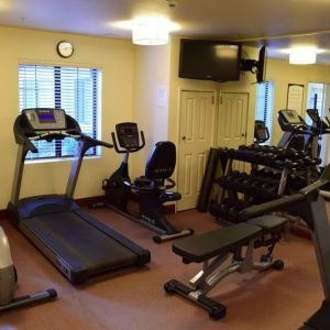 The fitness center of Sonesta ES Suites Portland Vancouver 41st Street has rows of free weights, a wall-mounted TV, and a variety of xercise machines.