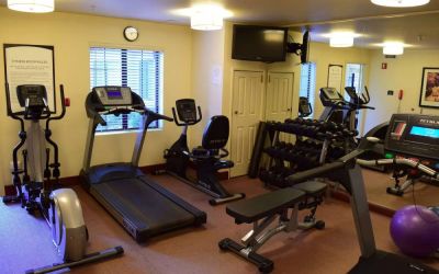 The fitness center of Sonesta ES Suites Portland Vancouver 41st Street has rows of free weights, a wall-mounted TV, and a variety of xercise machines.