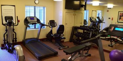 The fitness center of Sonesta ES Suites Portland Vancouver 41st Street has rows of free weights, a wall-mounted TV, and a variety of xercise machines.