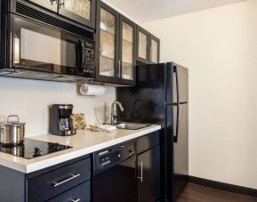Sonesta Simply Suites Salt Lake City Airport guest room kitchen, equipped with microwave, oven, and hob for cooking, and numerous cupboards and fridge-freezer for storage.