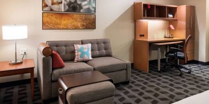 Guest room workspace in Sonesta Simply Suites Seattle Renton, featuring desk, lamp, and chair, with nearby sofa.
