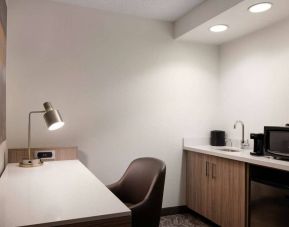 Guest room workspace in Sonesta Select Seattle Renton, including desk, chair, and lamp, with kitchenette nearby.