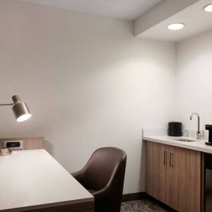 Guest room workspace in Sonesta Select Seattle Renton, including desk, chair, and lamp, with kitchenette nearby.